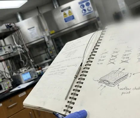Research notebook with handwritten data, equipment background visible behind it